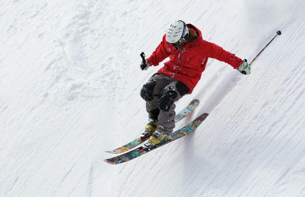 A skier in a red jacket descends a steep snowy slope, showcasing skill and adventure in winter sports.