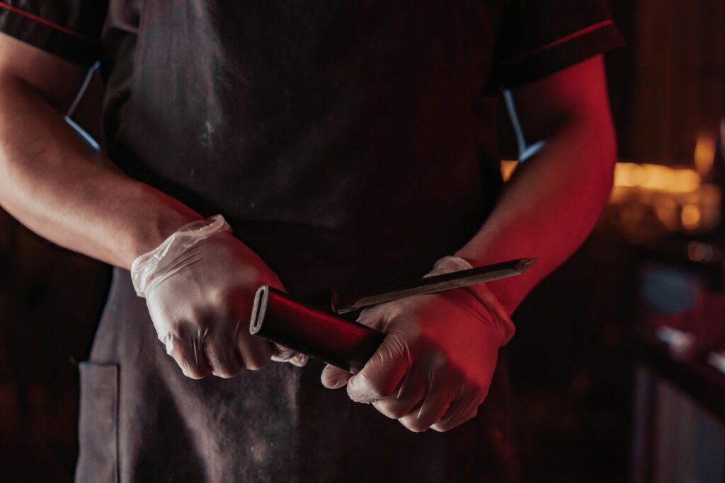 Close-up of a chef sharpening a knife indoors with dramatic red lighting, creating a moody atmosphere.