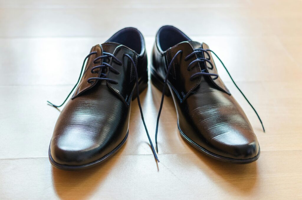 A pair of shiny, elegant black leather dress shoes with laces on a wooden floor.