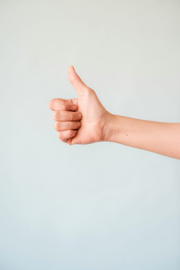 A close-up view of a hand showing a thumbs up against a plain background.