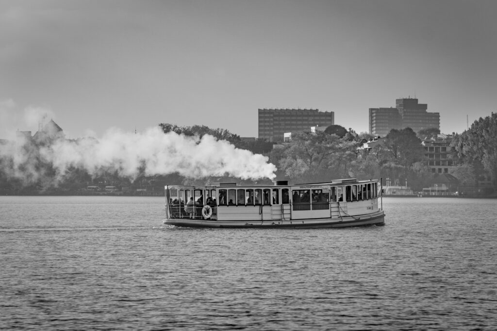 Black and white photo of a steaming ferry cruising through Hamburg, Germany's scenic waterways.