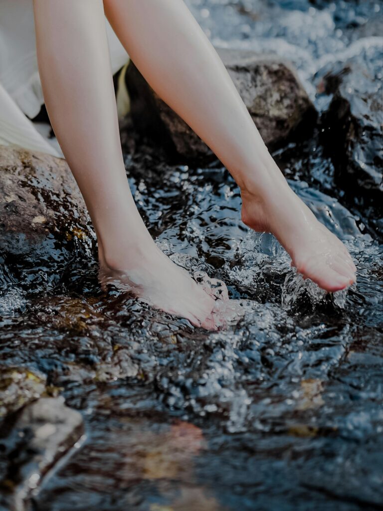 Close-up of a woman's feet splashing in a refreshing mountain stream during summer.