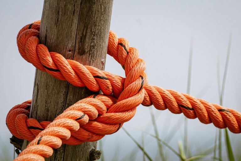 Detailed view of a bright orange rope tied securely around a weathered wooden post in an outdoor setting.