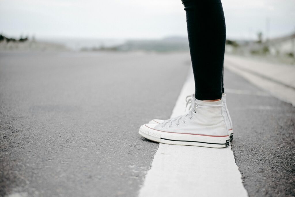 Close-up of white sneakers on a road, highlighting casual style and travel theme.