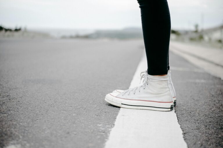 Close-up of white sneakers on a road, highlighting casual style and travel theme.