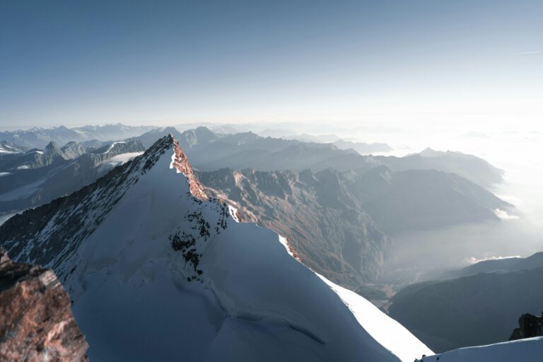 Breathtaking view of a snow-covered mountain peak with a vast landscape at sunrise, highlighting natural beauty.