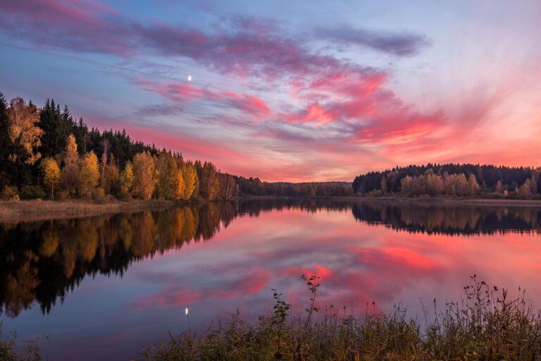Serene lake reflecting colorful sunset skies and autumn trees in a tranquil countryside setting.